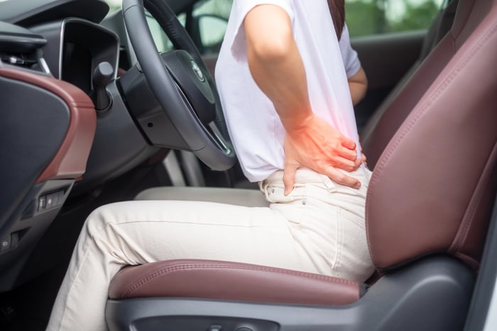 Driver with highlighted lower back pain while seated behind the wheel