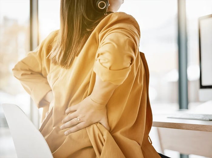 Woman seated at a desk pressing a hand to her aching hip