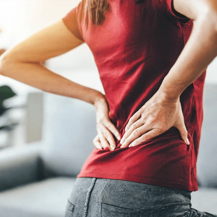Woman standing and holding her lower back and hip in discomfort