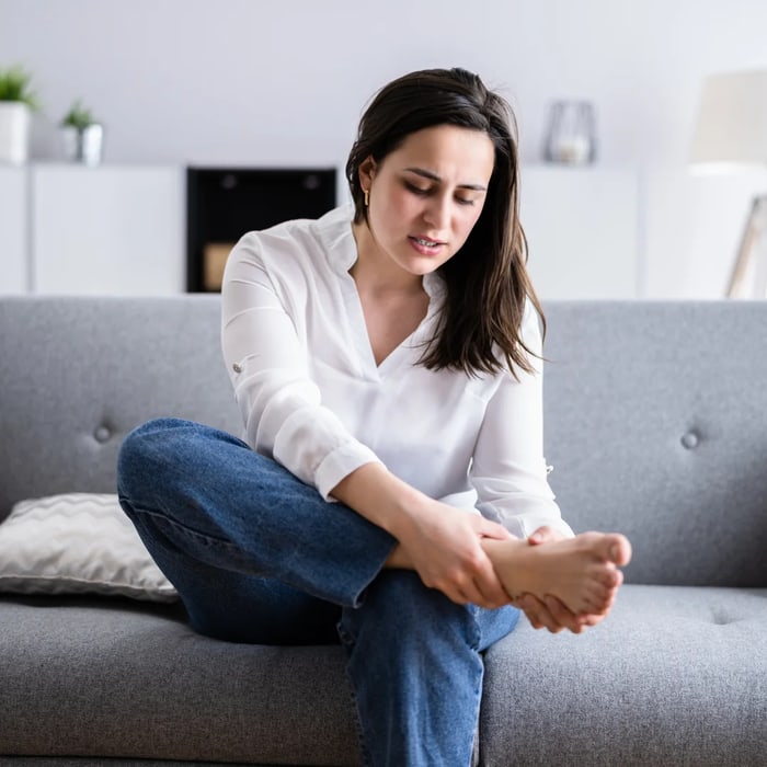 Woman seated on a sofa massaging her numb, tingling foot