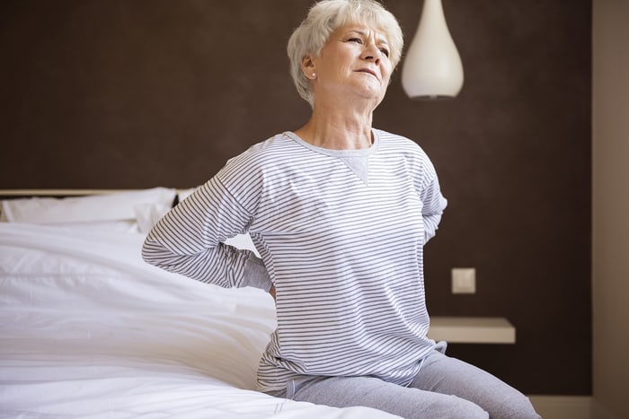 Woman sitting on the edge of her bed holding her lower back in the morning
