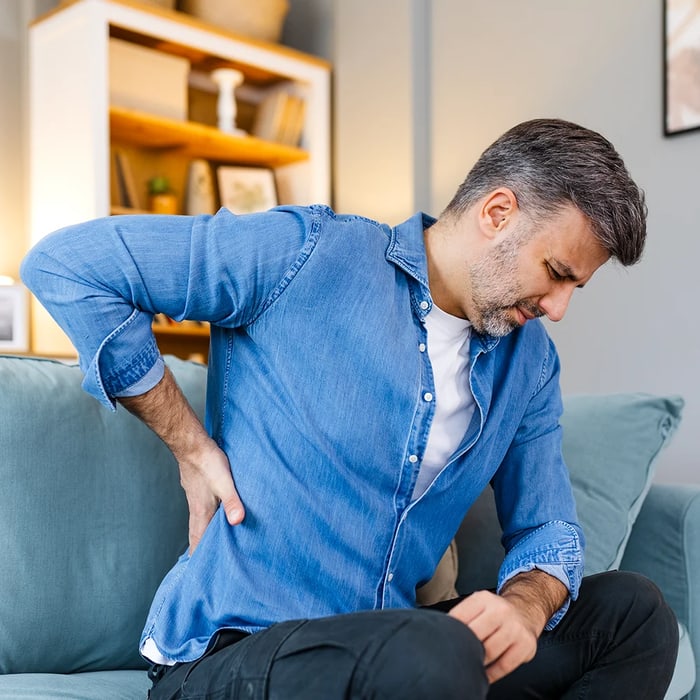 Man on a sofa pressing a hand to his painful lower back