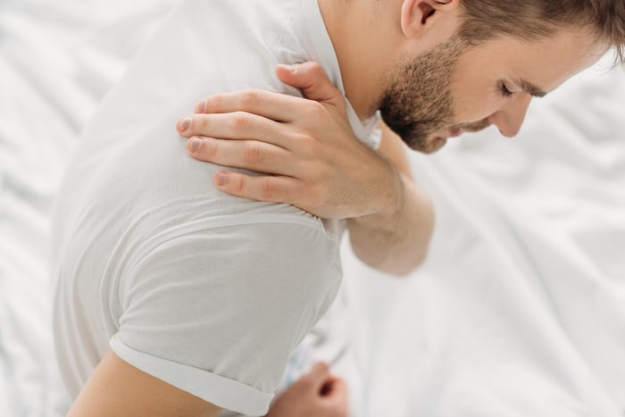 Man reaching across his chest to hold a painful shoulder