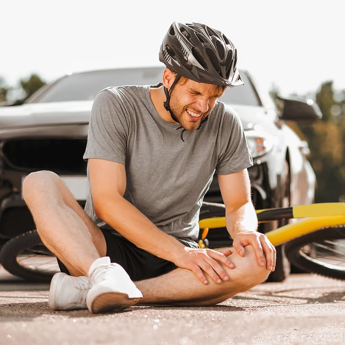 Cyclist sitting on the ground holding an injured knee beside his bike