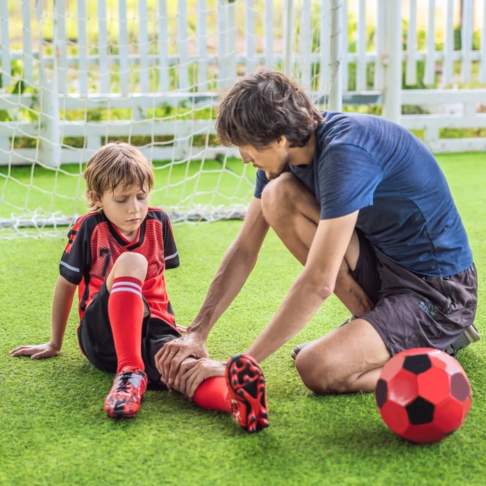 Coach helping a young soccer player with an injured ankle on the field