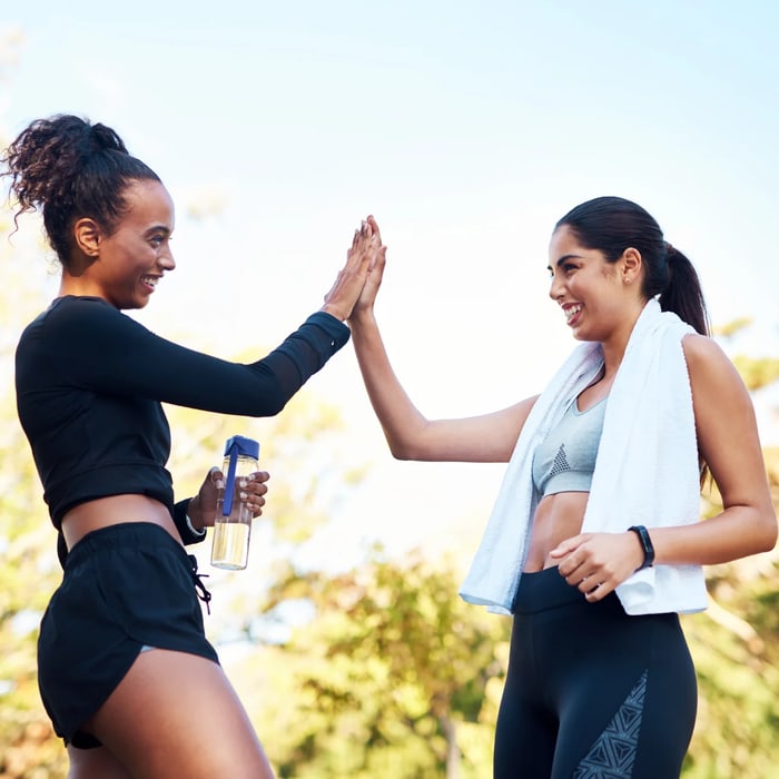 Two women high-fiving outdoors after a workout