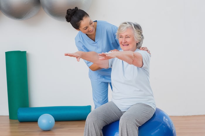 Provider guiding a smiling senior patient through a balance exercise on a stability ball