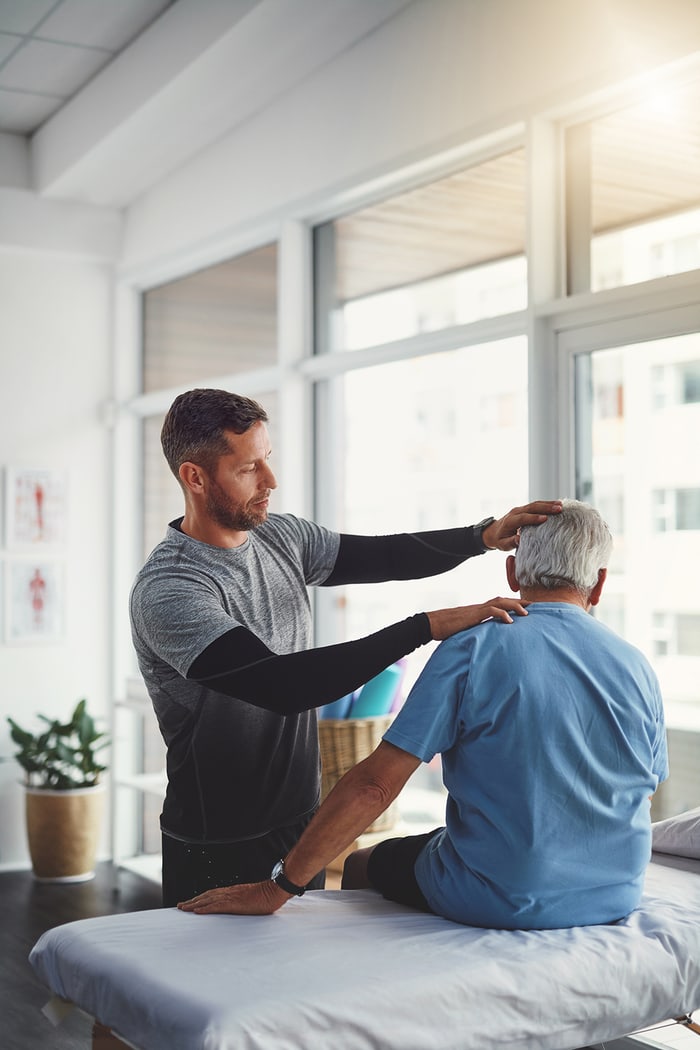Chiropractor performing a seated neck adjustment on an older patient in a bright treatment room