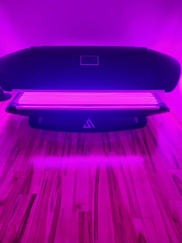 Vita Light Therapy Bed glowing with red and blue light, its full-body canopy raised over the padded bed